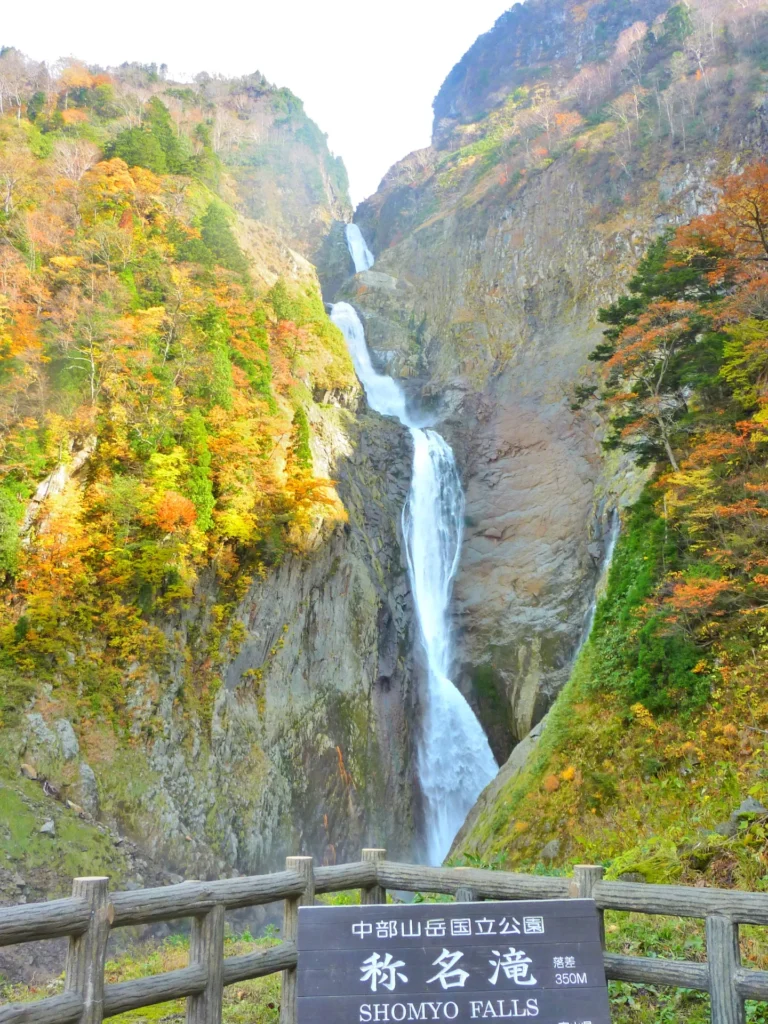 秋の称名滝展望台からの眺め。渓谷一帯が赤や黄色の紅葉に染まり、滝の白い流れと紅葉のコントラストが鮮やかに映えている写真