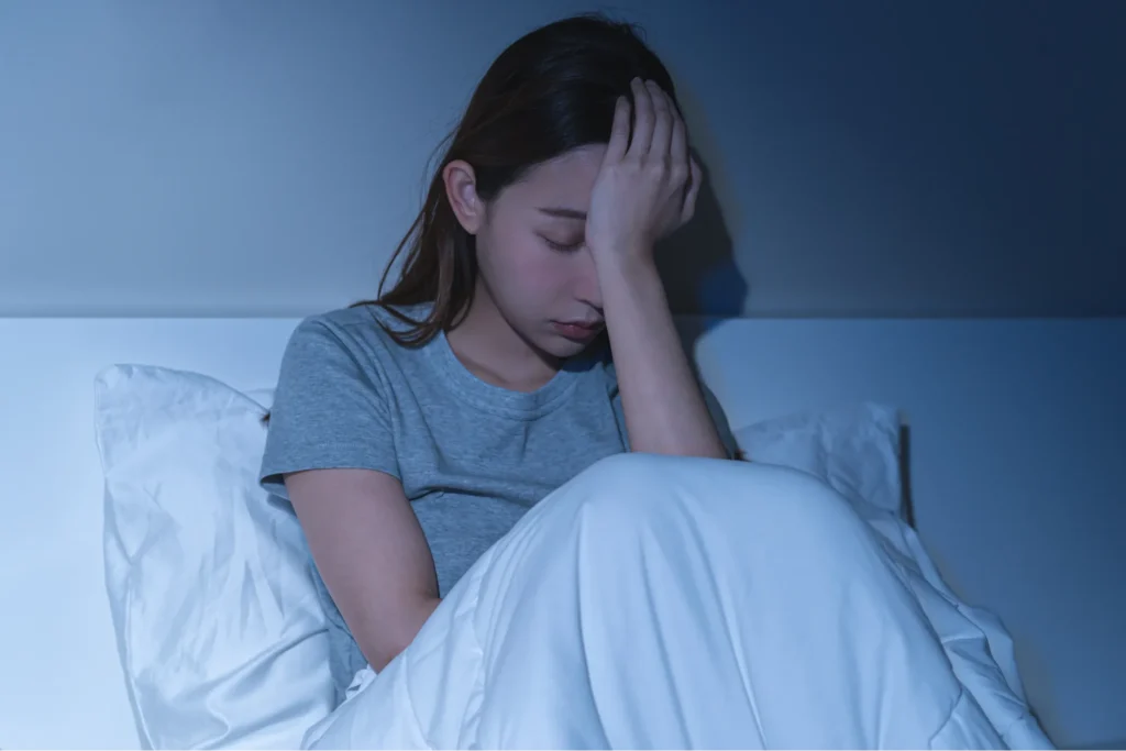 夜、避難所の布団で不安そうに頭を抱える女性